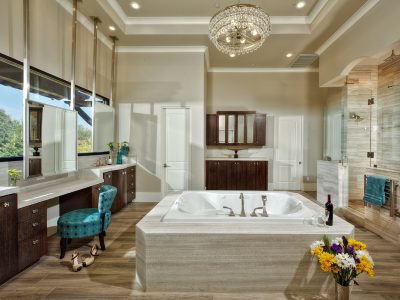 This sophisticated, transitional style bathroom features an open plan with huge windows that set the backdrop for the mirrors at the vanity, inviting the calm of the outdoors into the classy space. The bowed vanity cabinets, along with the crystal chandelier, add an element of elegance to this already comfortable space.