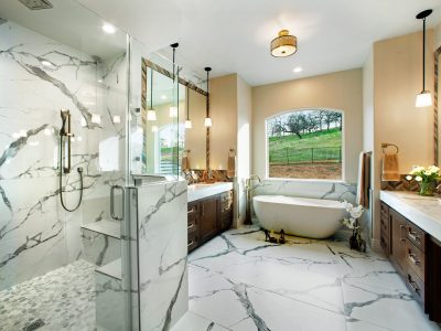 This modern bathroom provides the owner with a free-standing tub, large shower with handheld and rain shower heads, and two vanities with a make-up area. The warm tone chevron tile and walnut cabinets add a warm feeling to the marble-like large format tile. The unique materials and lighting fixtures displayed through its wall hanging pendants, mirror inserts, and drop-down quartz countertop.